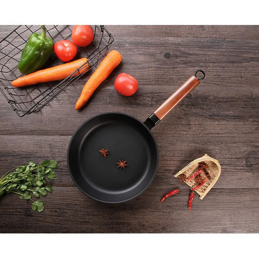 Wok KUROKO noir vu du dessus, avec manche en bois et deux étoiles de badiane, entouré de légumes.