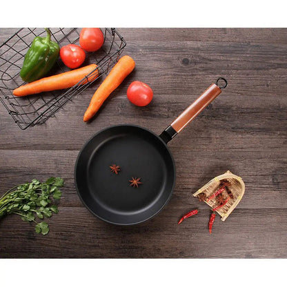 Wok KUROKO noir vu du dessus, avec manche en bois et deux étoiles de badiane, entouré de légumes.
